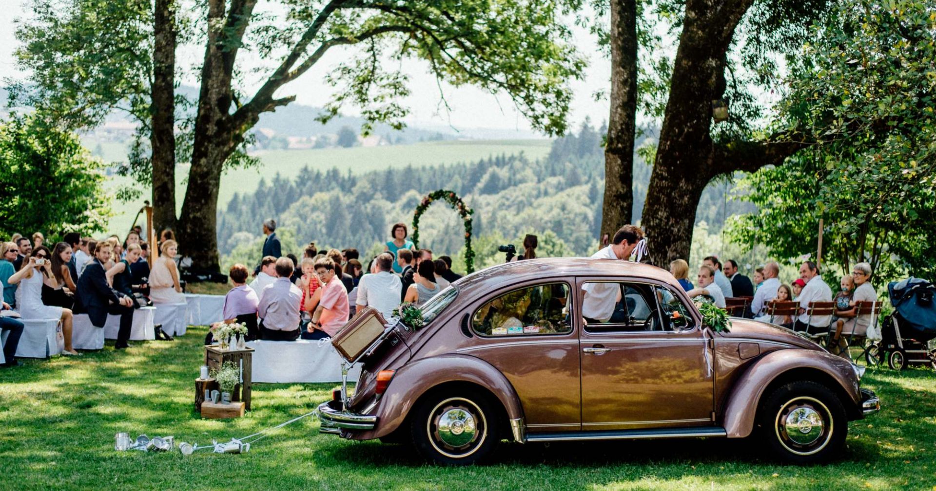 Hochzeitsgesellschaft mit VW Käfer im Vordergrund